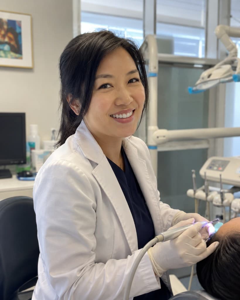 Smiling dentist in a white coat treating a patient in a modern dental office