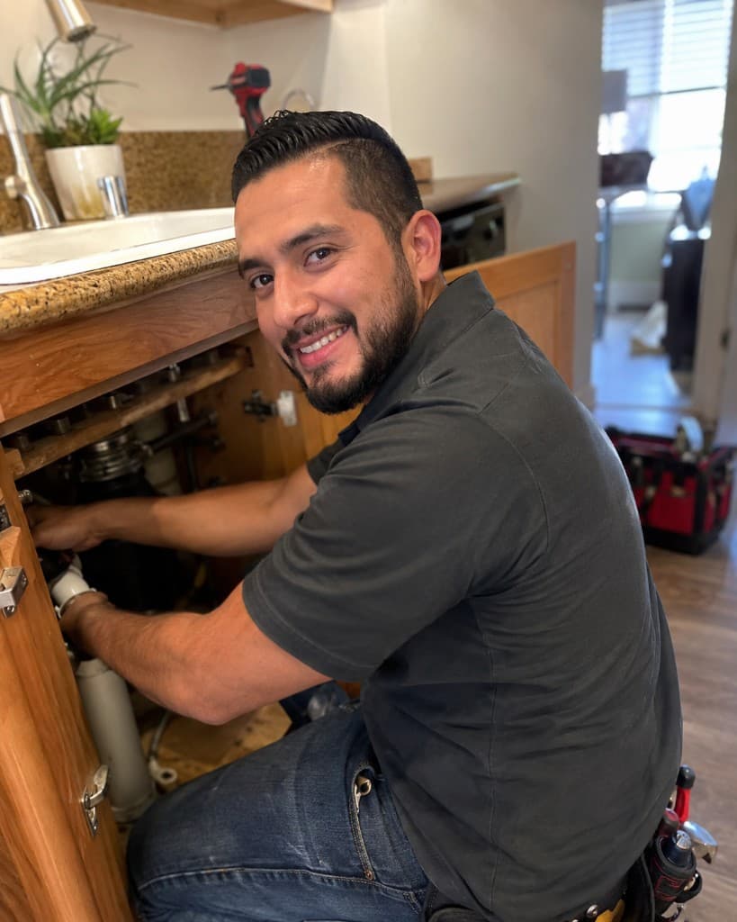 Smiling plumber repairing under-sink pipes in a residential kitchen